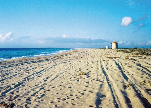 Un tratto panoramico della vasta spiaggia di Agios Ioannis, che si estende per circa 7 km, con i tradizionali mulini a vento che aggiungono un tocco distintivo al paesaggio.